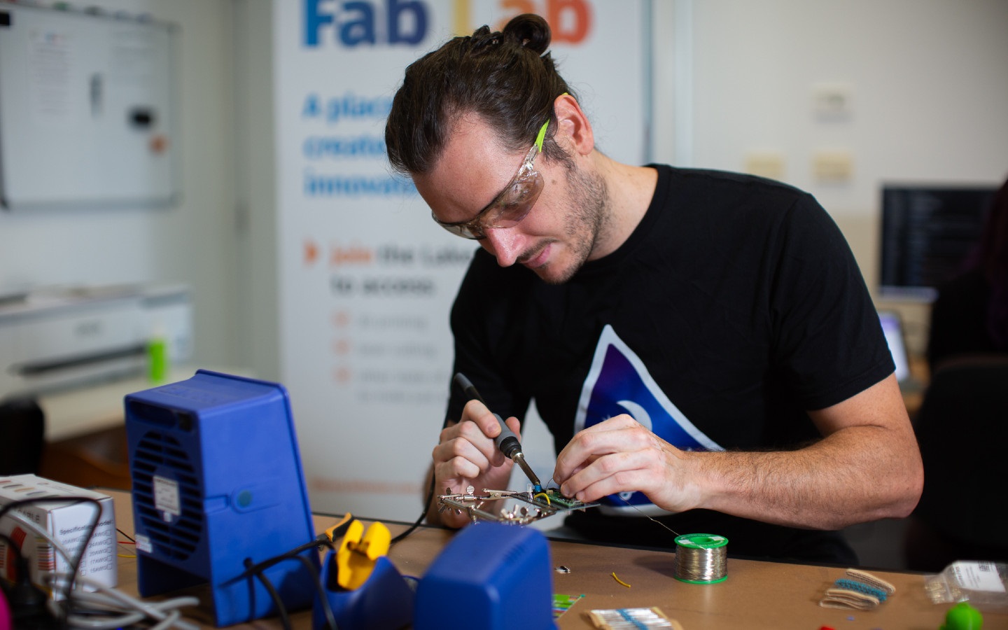 A man uses a soldering tool on a circuit board. 