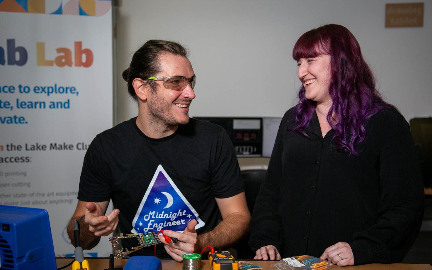 A man wearing safety glasses and a woman sitting a table.